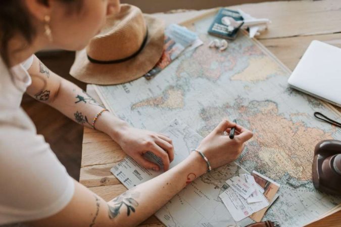 Une voyageuse trace son itinéraire sur une carte du monde posée sur une table en bois.