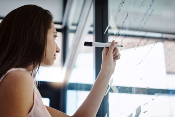 Une femme écrit des notes sur un tableau blanc pour organiser ses projets futurs.